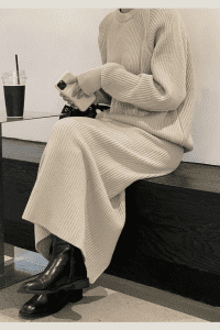 Woman in a beige ribbed knit sweater and matching skirt set, sitting in a café. Styled with black leather boots and a neutral-toned coffee aesthetic. Effortless modest fall outfit in a soft monochrome palette.