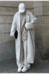 Casual modest fall outfit with an oversized cream wool coat, matching pants, hoodie, and white cap. Street-style neutral outfit for cold days, styled with sneakers and a relaxed silhouette.